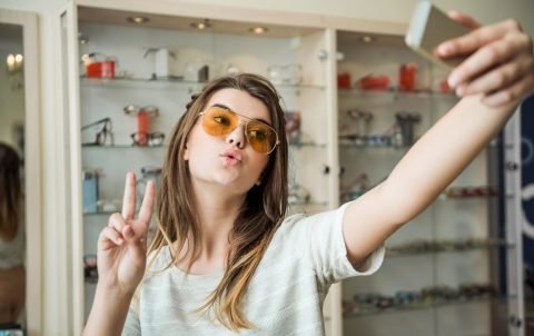 stylish-feminine-young-female-student-optician-store-making-glamorous-face-showing-v-sign-while-taking-selfie-new-pair-trendy-sunglasses_176420-3482