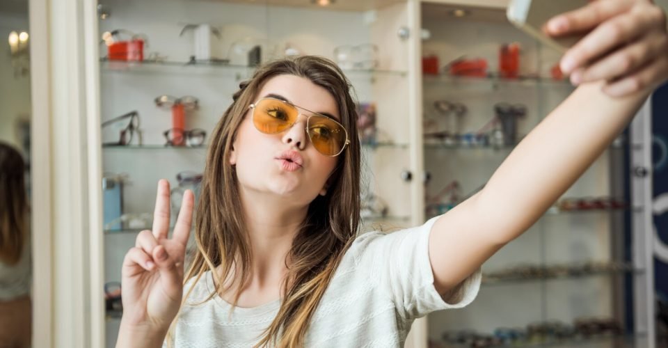 stylish-feminine-young-female-student-optician-store-making-glamorous-face-showing-v-sign-while-taking-selfie-new-pair-trendy-sunglasses_176420-3482
